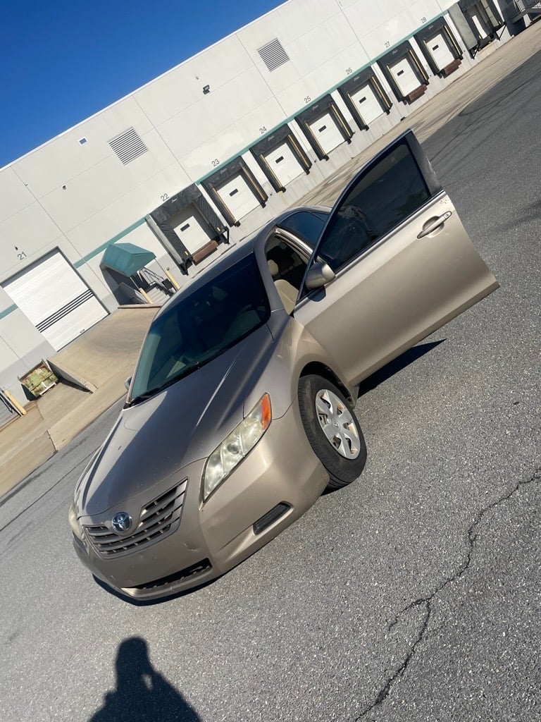 Tan-colored sedan parked in front of a white warehouse building with rows of loading doors on a sunny day